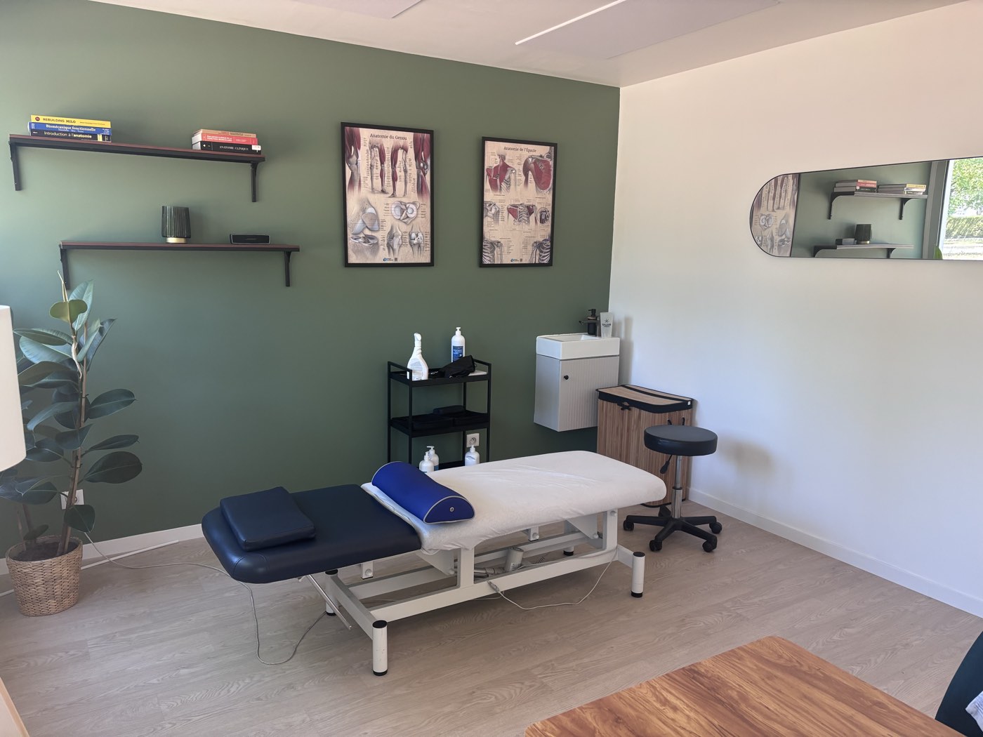 Une salle de soins au mur vert sauge, avec sa table de traitement et ses planches anatomiques